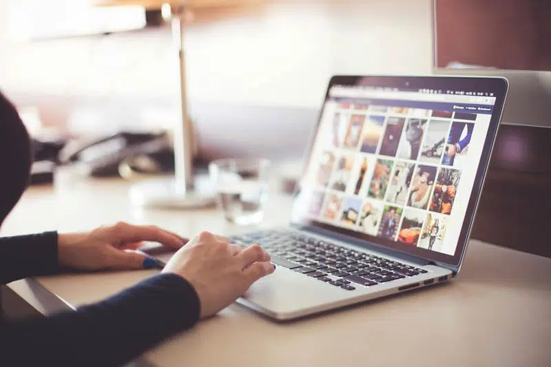 A Complete Guide to Building a Strong SEO Strategy Using the Four Pillars 28 SEO Strategy A person engrossed in digital marketing projects, using a laptop with multiple images displayed on the screen, is seated at a desk with a glass of water and a lamp in the background.